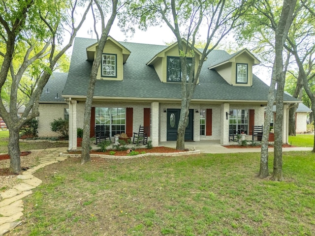 new england style home featuring roof with shingles, a front lawn, and brick siding