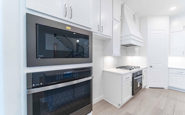 kitchen featuring custom exhaust hood, stainless steel appliances, light countertops, light wood-style floors, and white cabinetry