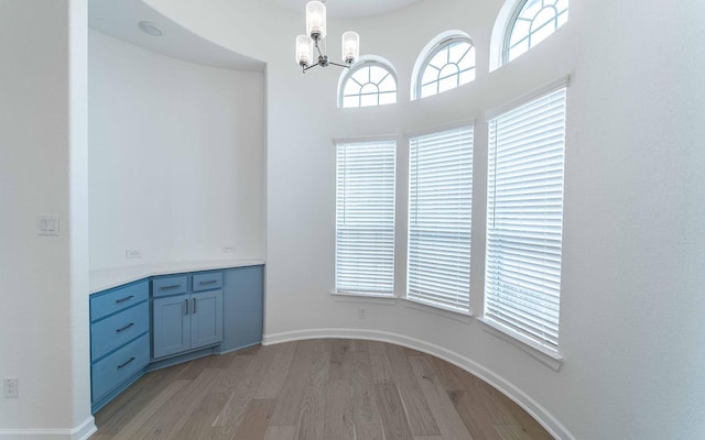 unfurnished dining area featuring a chandelier, light wood-style flooring, and baseboards