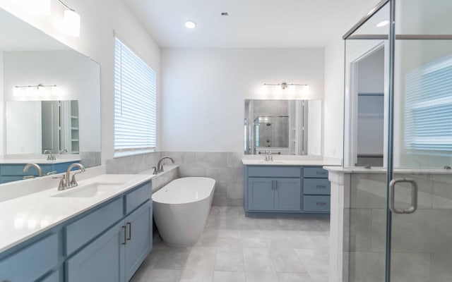 full bathroom featuring plenty of natural light, a stall shower, two vanities, and a sink