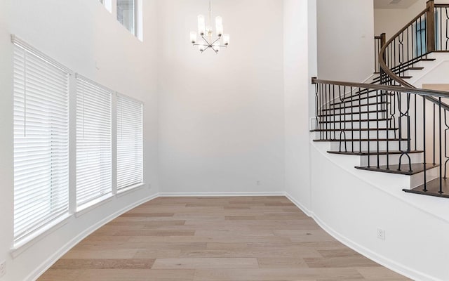 interior space featuring a notable chandelier, a towering ceiling, light wood-style flooring, and baseboards