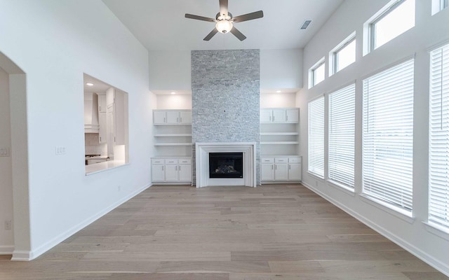 unfurnished living room with visible vents, baseboards, light wood-style flooring, ceiling fan, and a stone fireplace