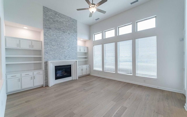 unfurnished living room with a high ceiling, light wood finished floors, a fireplace, and visible vents