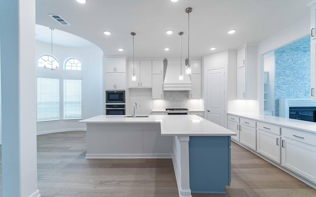 kitchen with decorative light fixtures, light countertops, a sink, black microwave, and premium range hood