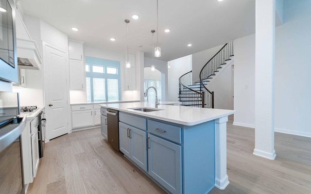 kitchen featuring stainless steel appliances, light countertops, hanging light fixtures, a kitchen island with sink, and a sink