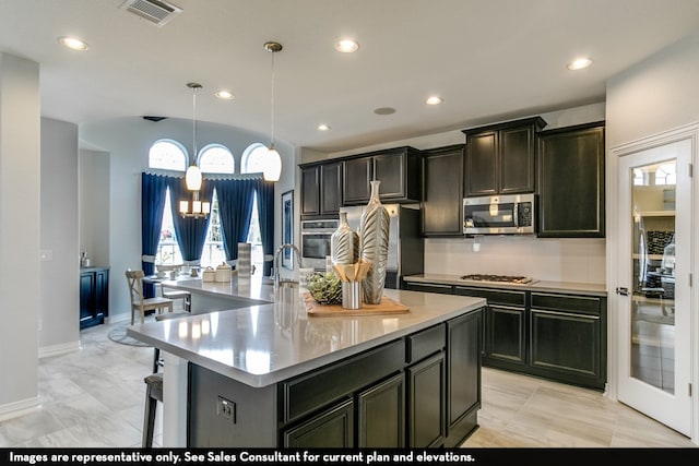 kitchen with a notable chandelier, an island with sink, pendant lighting, decorative backsplash, and appliances with stainless steel finishes