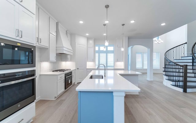 kitchen with an island with sink, light countertops, white cabinetry, pendant lighting, and a sink