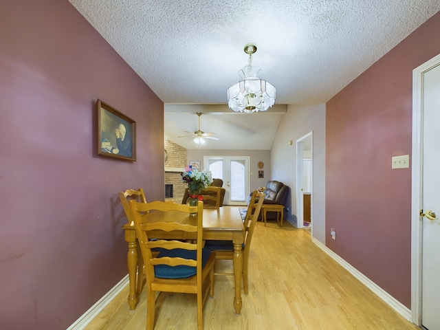 dining area with lofted ceiling, ceiling fan with notable chandelier, a brick fireplace, a textured ceiling, and light hardwood / wood-style floors