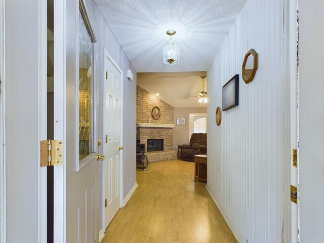 corridor with lofted ceiling, a textured ceiling, brick wall, and light hardwood / wood-style flooring