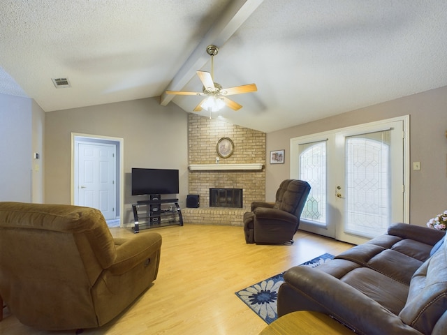 living room featuring lofted ceiling with beams, ceiling fan, light wood-type flooring, a textured ceiling, and a fireplace