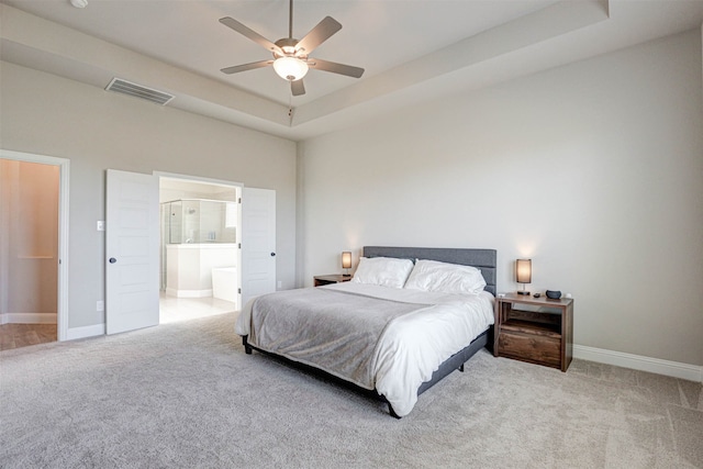 bedroom with ceiling fan, a raised ceiling, light colored carpet, and ensuite bathroom