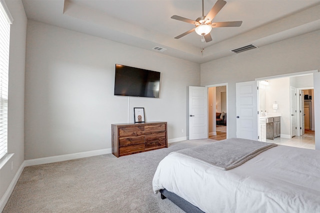 carpeted bedroom featuring a tray ceiling, ensuite bathroom, and ceiling fan