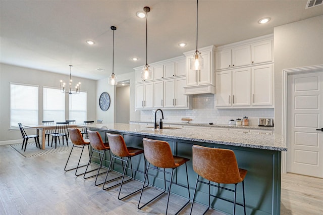 kitchen with white cabinets, decorative light fixtures, a spacious island, and sink