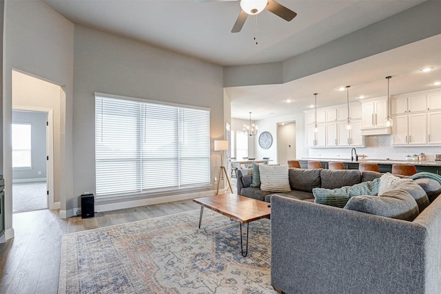 living room featuring ceiling fan with notable chandelier, light hardwood / wood-style flooring, a wealth of natural light, and sink