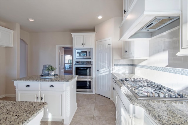 kitchen featuring custom exhaust hood, white cabinets, tasteful backsplash, light stone counters, and stainless steel appliances