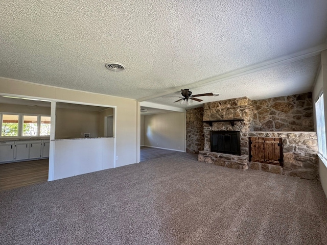 unfurnished living room featuring ceiling fan, dark carpet, a stone fireplace, and a textured ceiling