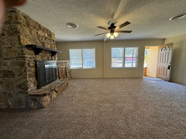 unfurnished living room with carpet flooring, ceiling fan, a stone fireplace, and a textured ceiling