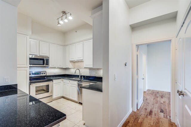 kitchen with decorative backsplash, appliances with stainless steel finishes, light wood-type flooring, sink, and white cabinets