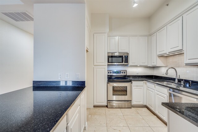 kitchen featuring backsplash, dark stone counters, sink, appliances with stainless steel finishes, and white cabinetry