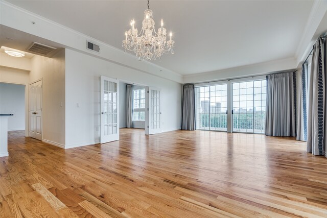 empty room featuring crown molding, light hardwood / wood-style flooring, french doors, and an inviting chandelier