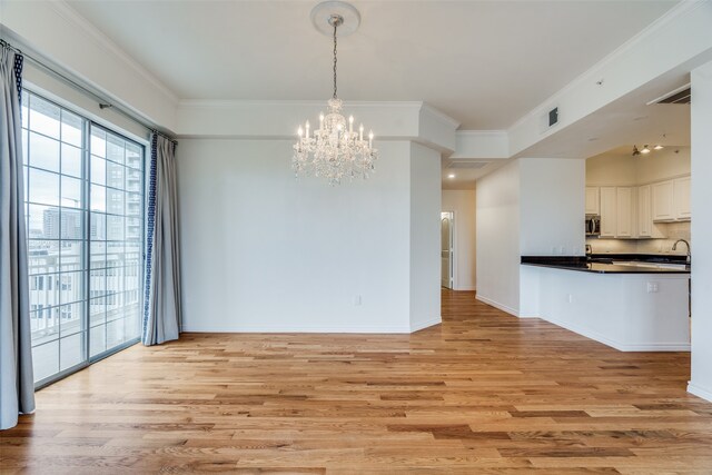 unfurnished dining area with ornamental molding, a notable chandelier, and light wood-type flooring