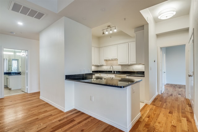 kitchen with kitchen peninsula, decorative backsplash, sink, light hardwood / wood-style floors, and white cabinetry