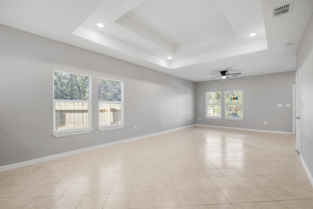 empty room with light tile patterned floors, a raised ceiling, and ceiling fan