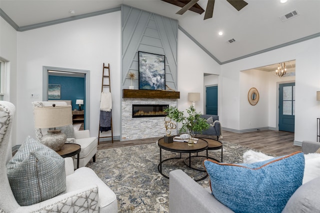 living room featuring a large fireplace, high vaulted ceiling, hardwood / wood-style floors, ceiling fan with notable chandelier, and ornamental molding