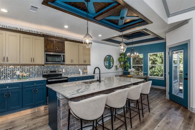 kitchen with a kitchen island with sink, crown molding, light wood-type flooring, appliances with stainless steel finishes, and decorative light fixtures