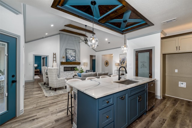 kitchen featuring a large fireplace, sink, blue cabinets, pendant lighting, and a center island with sink