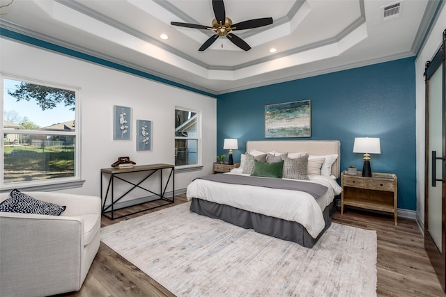 bedroom featuring a raised ceiling, ceiling fan, a barn door, ornamental molding, and wood-type flooring