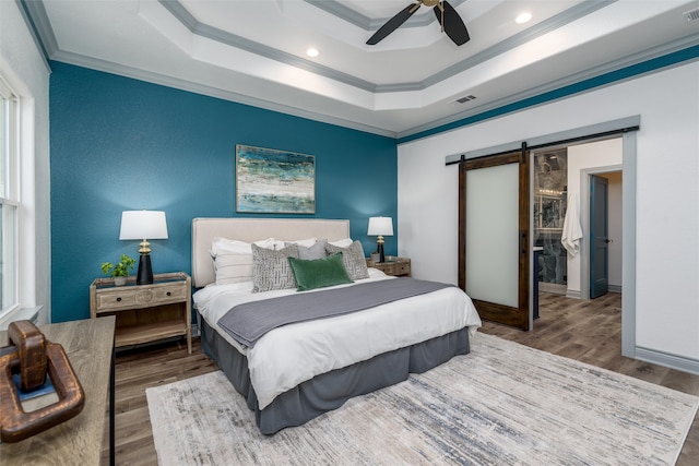 bedroom featuring ceiling fan, a raised ceiling, a barn door, crown molding, and hardwood / wood-style floors