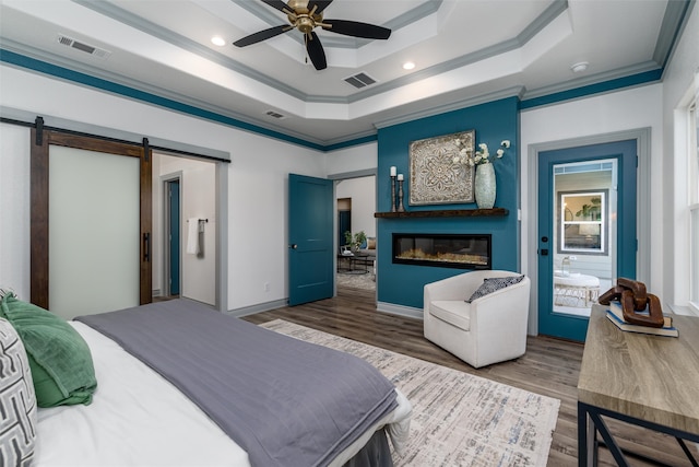 bedroom featuring ceiling fan, dark wood-type flooring, a raised ceiling, a barn door, and crown molding