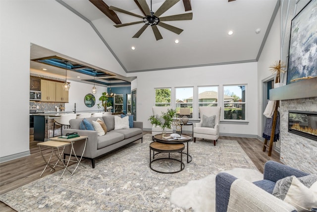 living room featuring ceiling fan with notable chandelier, light wood-type flooring, high vaulted ceiling, and a stone fireplace