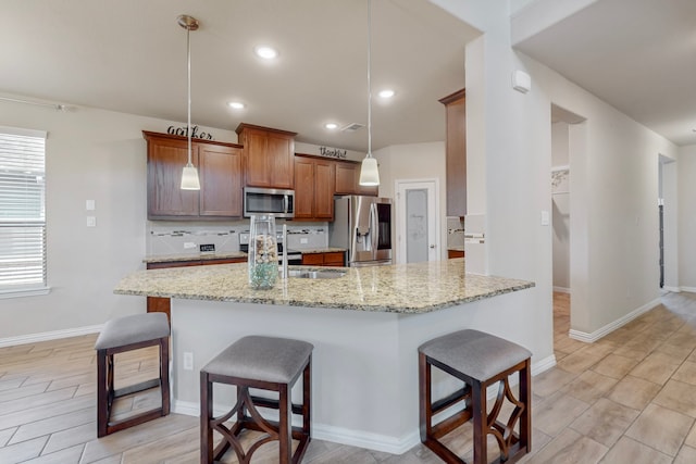 kitchen with pendant lighting, appliances with stainless steel finishes, tasteful backsplash, light stone countertops, and a kitchen bar