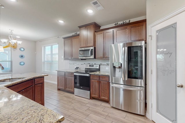 kitchen featuring sink, appliances with stainless steel finishes, an inviting chandelier, hanging light fixtures, and light stone countertops