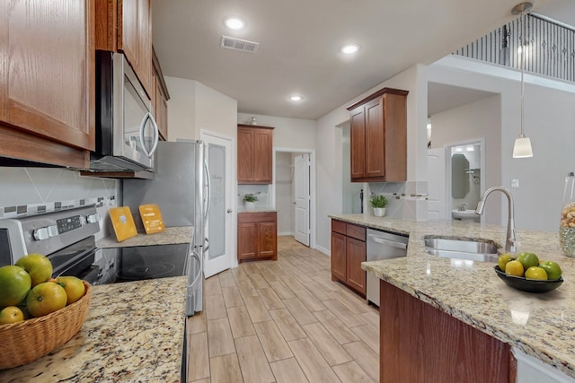 kitchen with pendant lighting, sink, appliances with stainless steel finishes, light stone counters, and light hardwood / wood-style floors