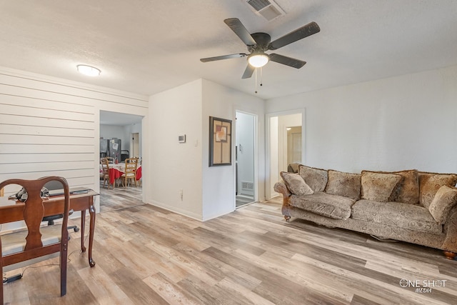 living room with ceiling fan, light wood-type flooring, and a textured ceiling