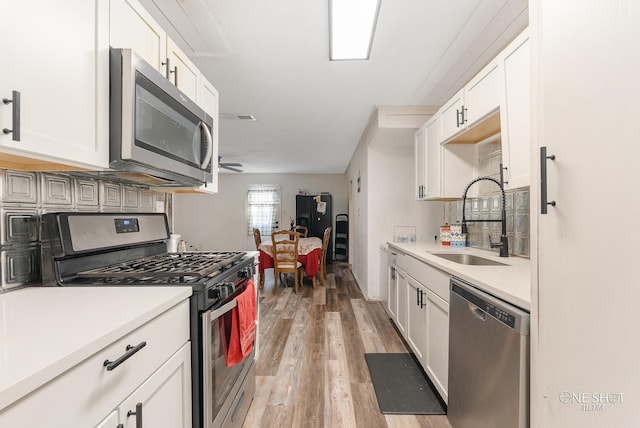 kitchen with appliances with stainless steel finishes, light wood-type flooring, white cabinetry, and sink