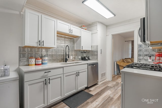 kitchen featuring white cabinetry, dishwasher, sink, backsplash, and light wood-type flooring