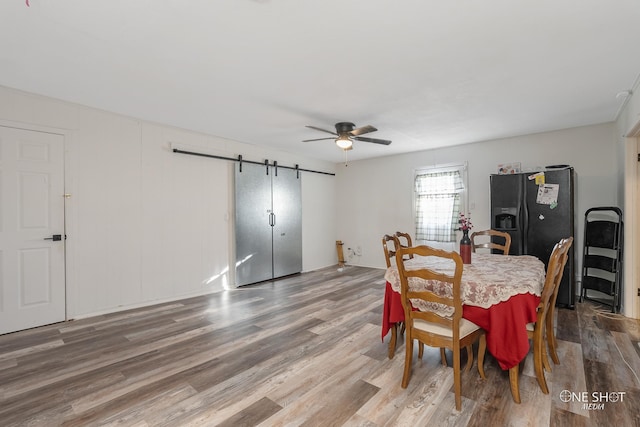 dining space with hardwood / wood-style floors, a barn door, and ceiling fan