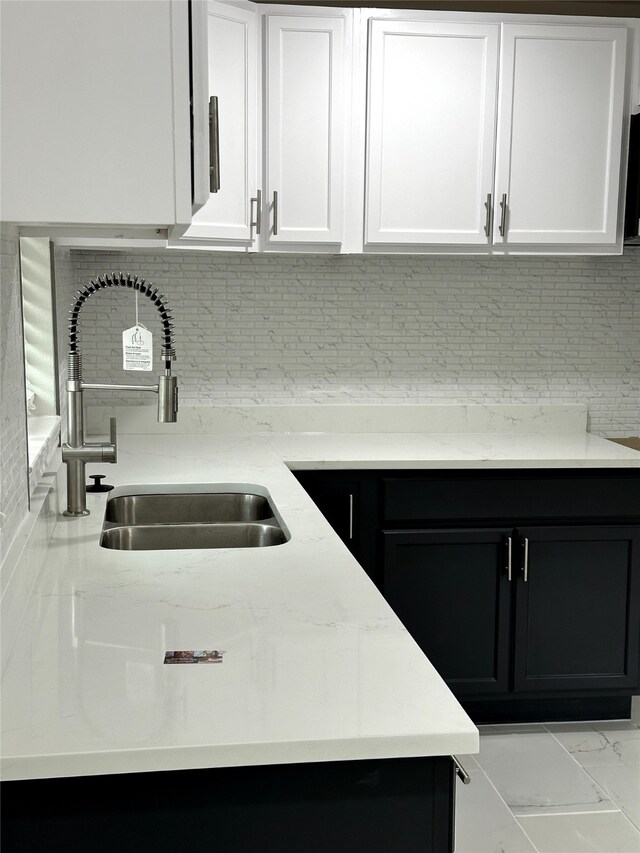 kitchen featuring white cabinets, backsplash, light stone countertops, and sink