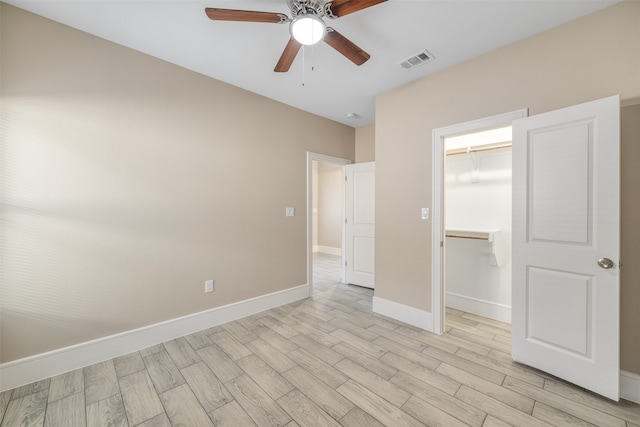 unfurnished bedroom featuring a walk in closet, ceiling fan, a closet, and light wood-type flooring