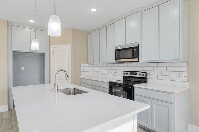 kitchen with a kitchen island with sink, sink, light wood-type flooring, decorative light fixtures, and stainless steel appliances