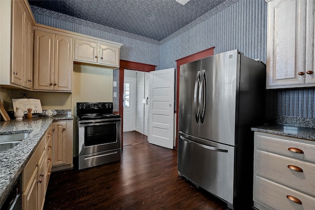 kitchen with dark wood-type flooring, appliances with stainless steel finishes, light brown cabinetry, and dark stone countertops