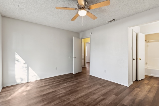 unfurnished bedroom featuring a textured ceiling, connected bathroom, ceiling fan, and dark wood-type flooring