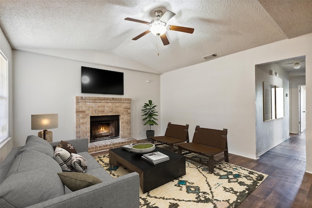 living room with a brick fireplace, vaulted ceiling, dark hardwood / wood-style floors, ceiling fan, and a textured ceiling