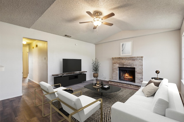 living room with vaulted ceiling, dark hardwood / wood-style floors, ceiling fan, a textured ceiling, and a fireplace