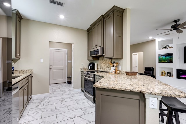 kitchen featuring light stone countertops, appliances with stainless steel finishes, a kitchen breakfast bar, ceiling fan, and built in features