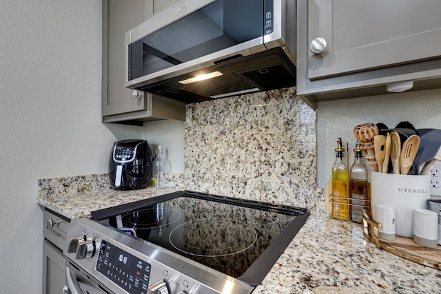 kitchen featuring decorative backsplash, range, gray cabinets, and light stone counters